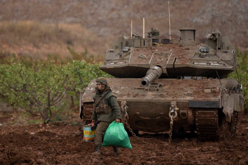 An Israeli soldier walks past a tank in an area near the Israeli-Lebanese border, as seen from ...