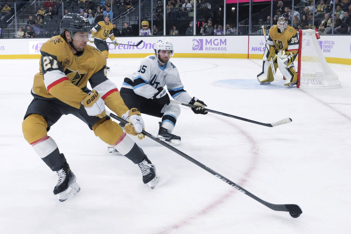 Vegas Golden Knights defenseman Shea Theodore (27) directs the puck behind the net while being ...