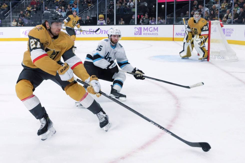 Vegas Golden Knights defenseman Shea Theodore (27) directs the puck behind the net while being ...