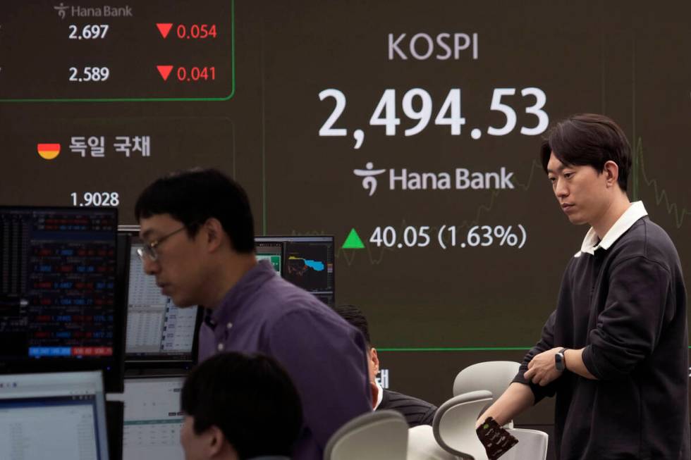 Currency traders work near a screen showing the Korea Composite Stock Price Index (KOSPI) at th ...