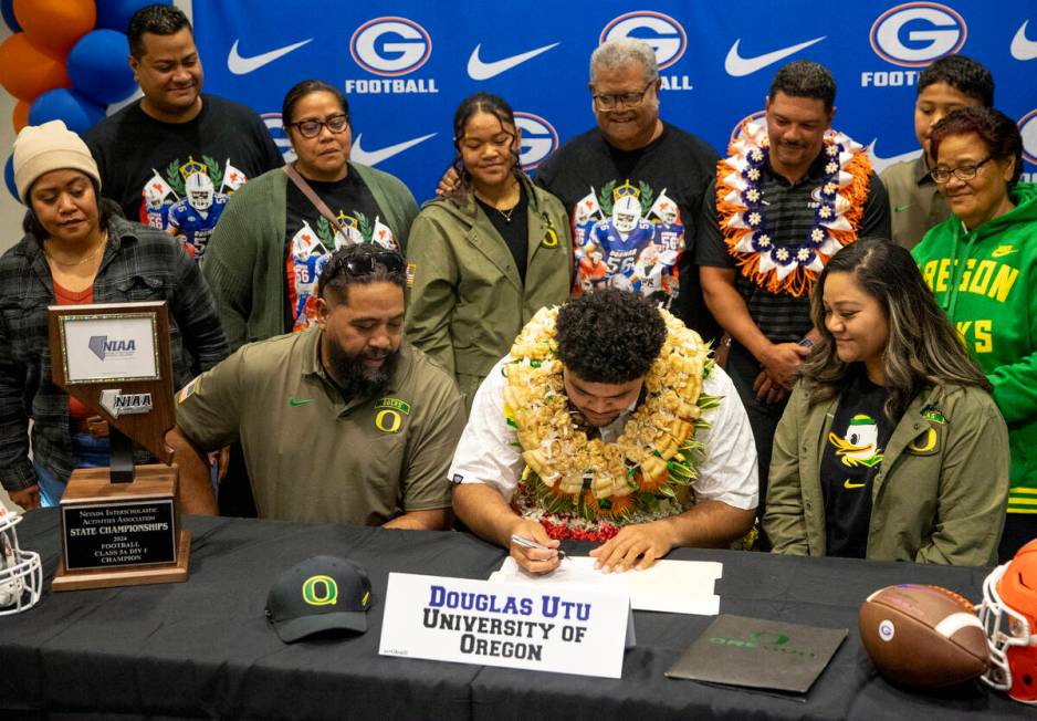 Bishop Gorman offensive lineman Douglas Utu, center, signs a financial aid agreement with the U ...