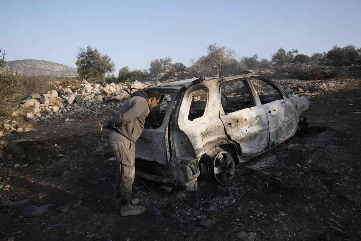 A Palestinian inspects the car that was targeted in an Israeli airstrike that the military said ...