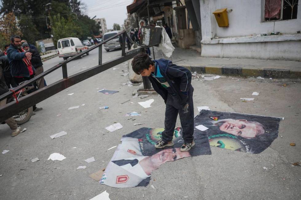 A boy steps over pictures of Syrian President Bashar Assad and his late father, Hafez Assad, ri ...