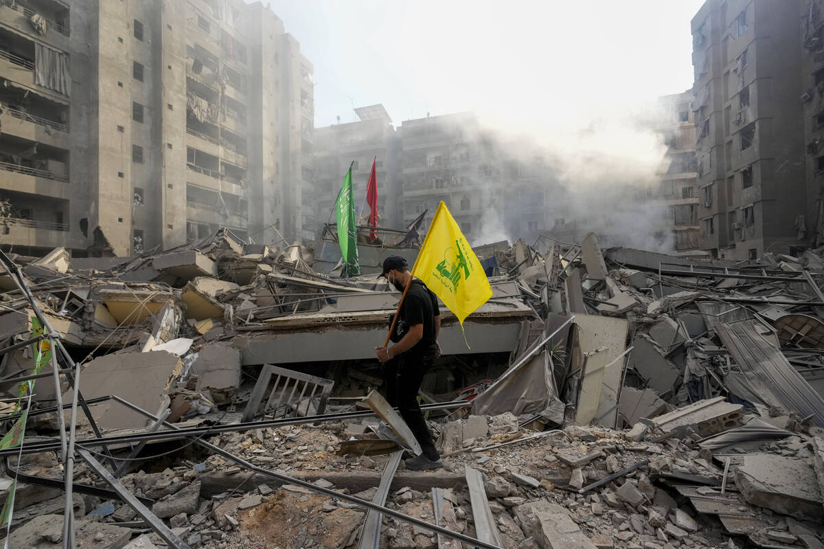 FILE - A man carries a Hezbollah flag as he walks on the rubble of his destroyed apartment foll ...