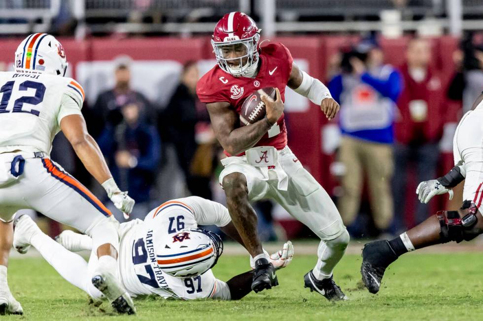 Alabama quarterback Jalen Milroe (4) eludes Auburn defensive lineman Quientrail Jamison-Travis ...