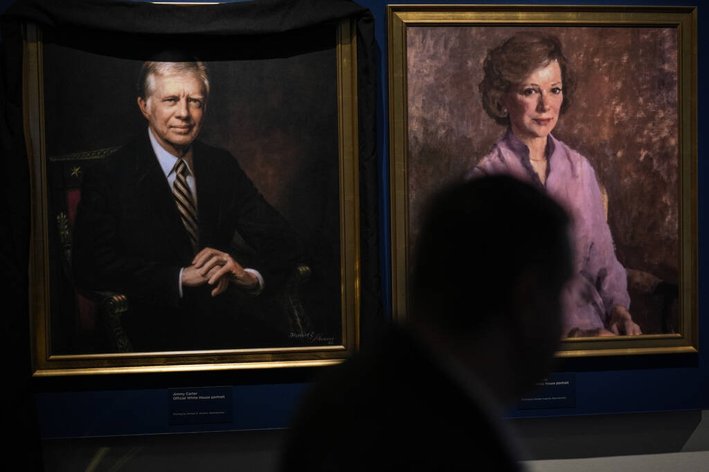 A man moves by the portrait of former President Jimmy Carter and his wife Rosalynn Carter at th ...