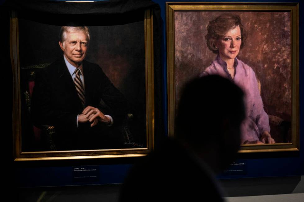 A man moves by the portrait of former President Jimmy Carter and his wife Rosalynn Carter at th ...