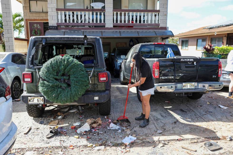 A woman sweeps debris from a driveway across the street from the home where a New Year's Eve fi ...