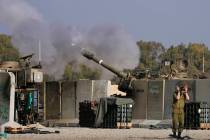 An Israeli soldier covers his ears as an artillery gunner fires into the Gaza Strip from a posi ...