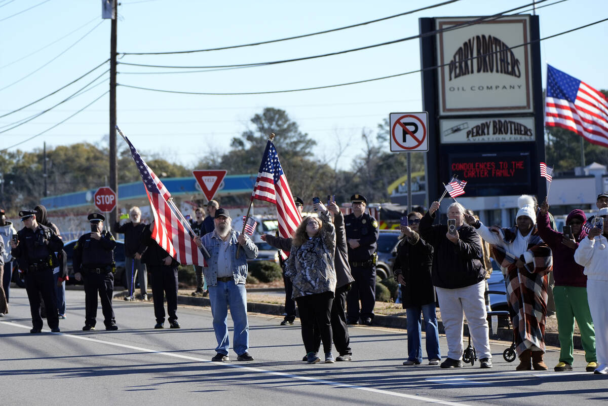 People line the road before the hearse with the casket of former President Jimmy Carter departs ...