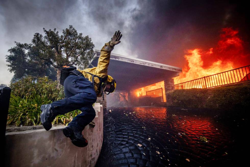 A firefighter jumps over a fence while fighting the Palisades Fire in the Pacific Palisades nei ...