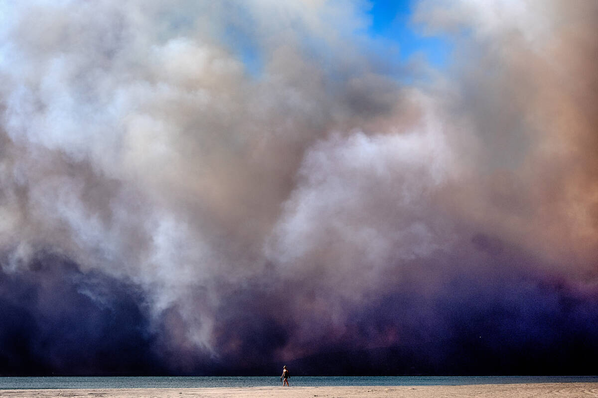 A lone beachgoer walks along the coast as a large dark plume of smoke passes over the beach fro ...