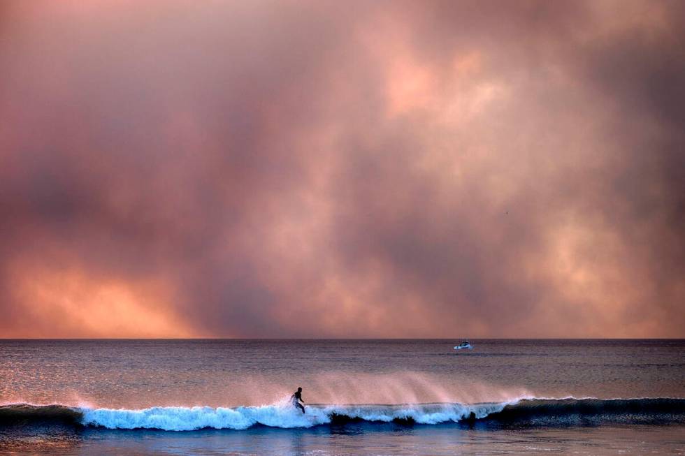 A surfer takes off on a wave under a blackened sky from the Palisades Fire in the Pacific Palis ...