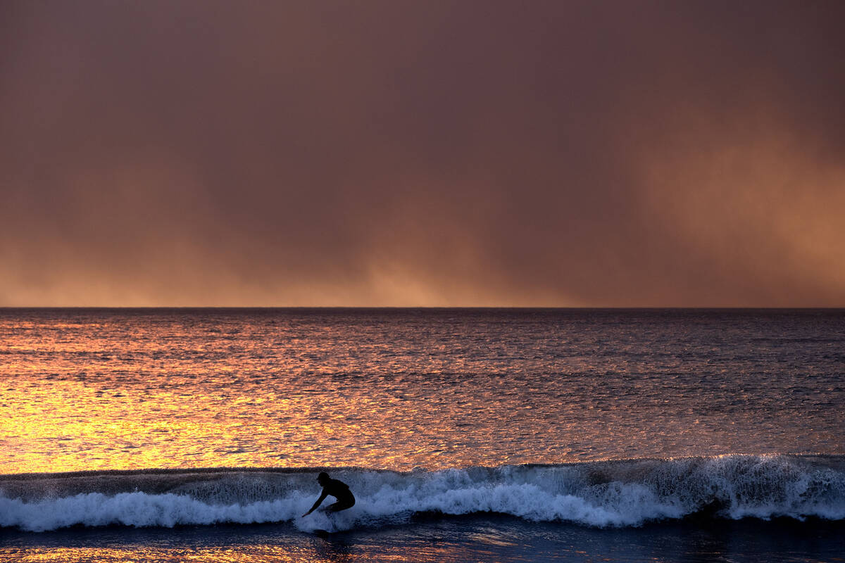 A surfer takes off on a wave under a blackened sky from the Palisades Fire in the Pacific Palis ...