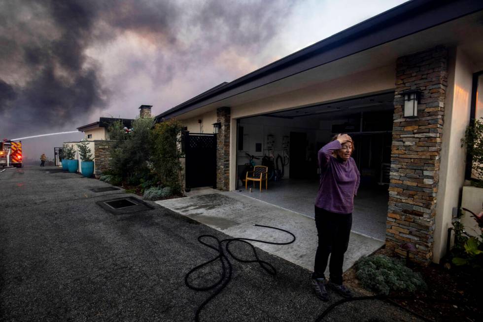 A resident stands in front of a garage as fire crews fight the Palisades Fire nearby in the Pac ...