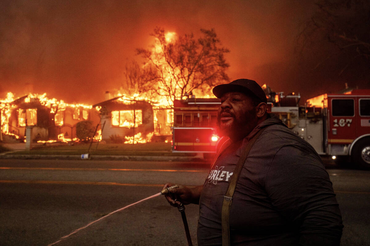 A resident sprays their property with a garden hose as the Eaton Fire engulfs structures across ...