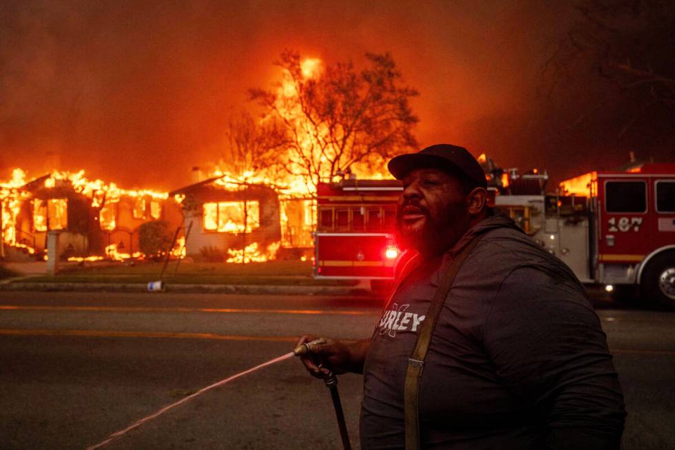 A resident sprays their property with a garden hose as the Eaton Fire engulfs structures across ...