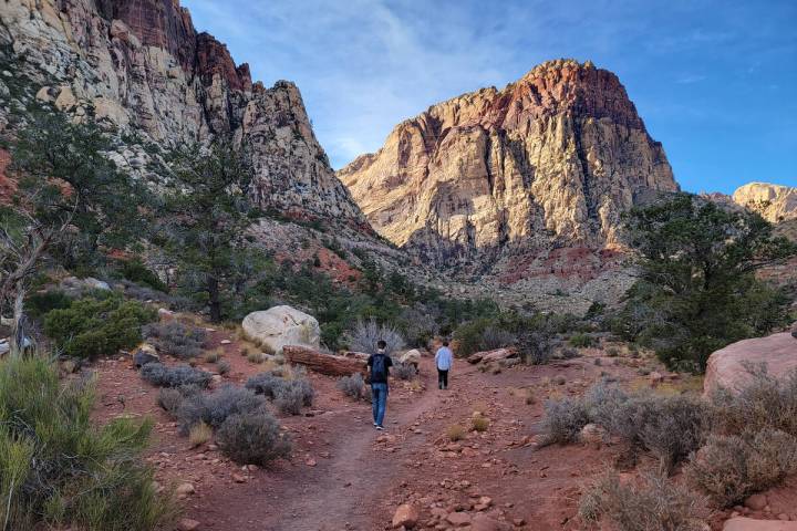 Hikers follow the South Oak Creek Trail toward the base of the red and beige sandstone cliffs o ...