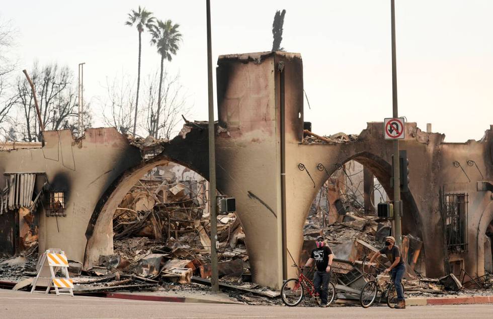 Cyclists move past a destroyed structure on Lake Avenue, Thursday, Jan. 9, 2025, in the downtow ...