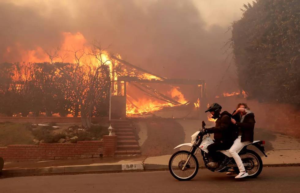 Two people ride past a burning house off Enchanted Way in the Marquez Knolls neighborhood of Pa ...