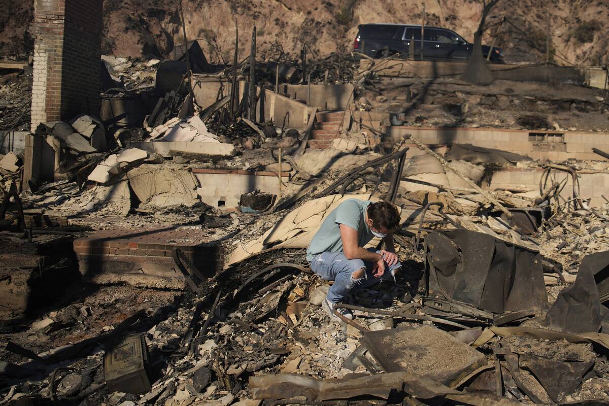 Luke Dexter kneels as he sifts through the remains of his father's fire-ravaged beach front pro ...