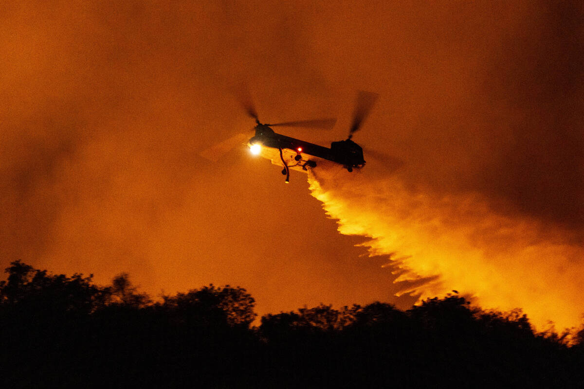 A helicopter drops water on the Palisades Fire in Mandeville Canyon, Saturday, Jan. 11, 2025, i ...