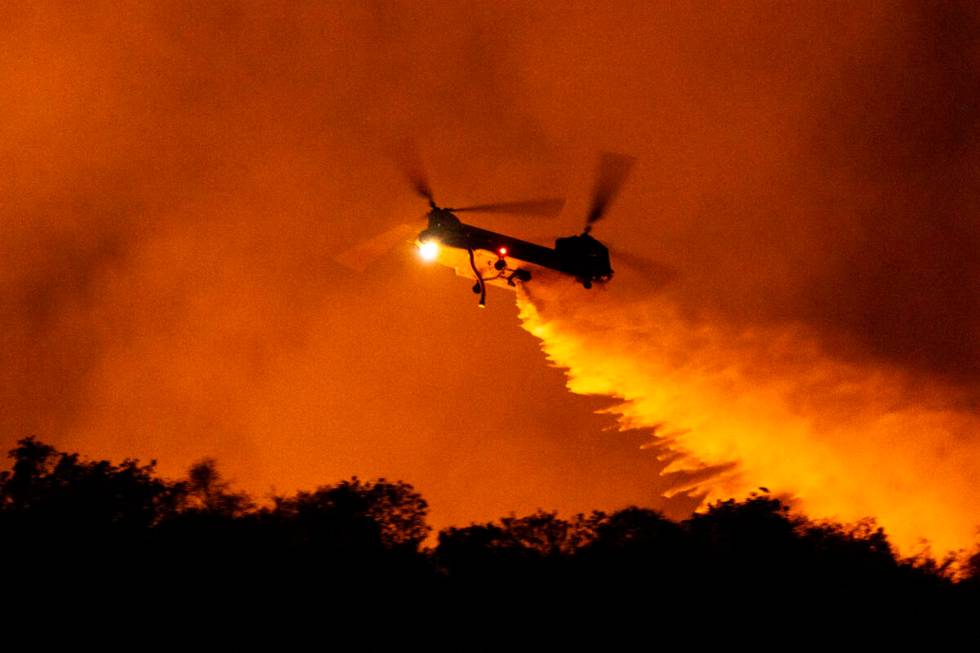 A helicopter drops water on the Palisades Fire in Mandeville Canyon, Saturday, Jan. 11, 2025, i ...