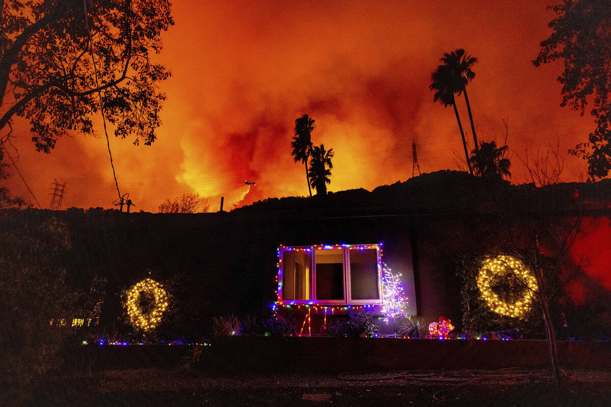 A helicopter drops water on the Palisades Fire behind a home with Christmas lights in Mandevill ...