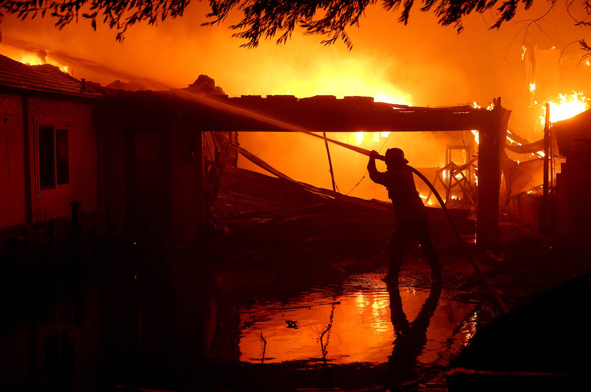 A firefighter sprays water on a burning home while battling the Eaton fire on Jan. 8, 2025, in ...