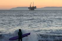 A surfer stands with offshore oil and gas platform Esther in the distance on Sunday, Jan. 5, 20 ...