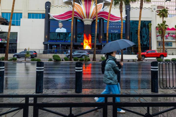 Pedestrians employ an umbrella for the first time in many months as they navigate the Strip whi ...